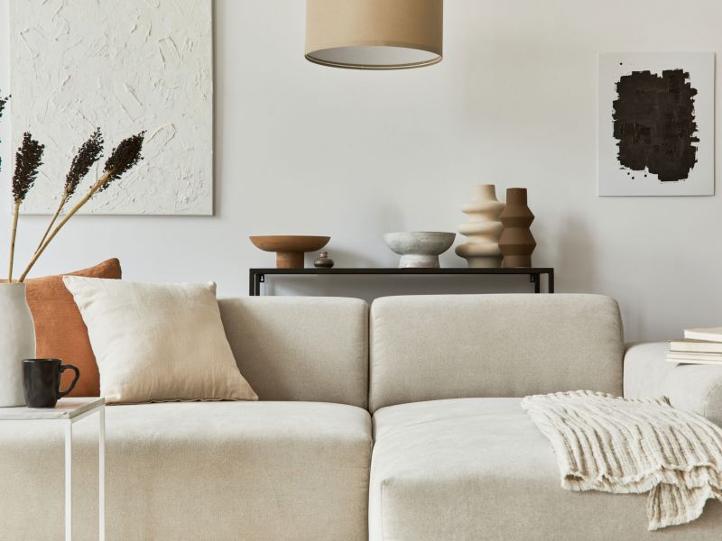 Modern living room with a beige sofa, neutral pillows, vases, wall art, and minimalistic decor.