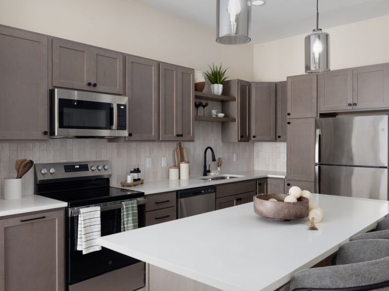 Modern kitchen with gray cabinets, stainless steel appliances, and a white island with bar stools.