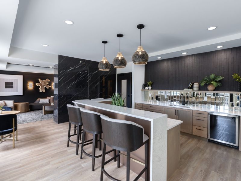 Modern kitchen with a large island, bar stools, pendant lights, and sleek black and wood accents.