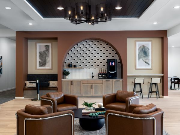 Modern lounge with brown leather chairs, a coffee station, and abstract art on the walls.