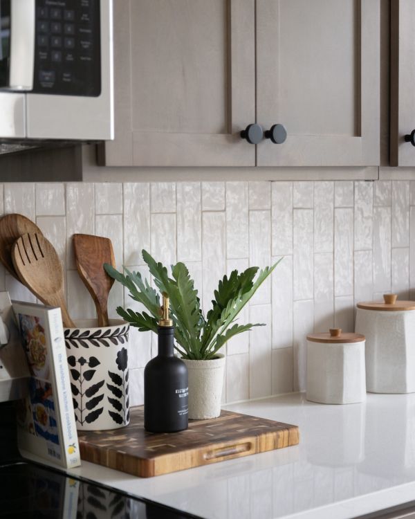 A modern kitchen counter with a plant, utensils, cookbook, olive oil bottle, and ceramic canisters.
