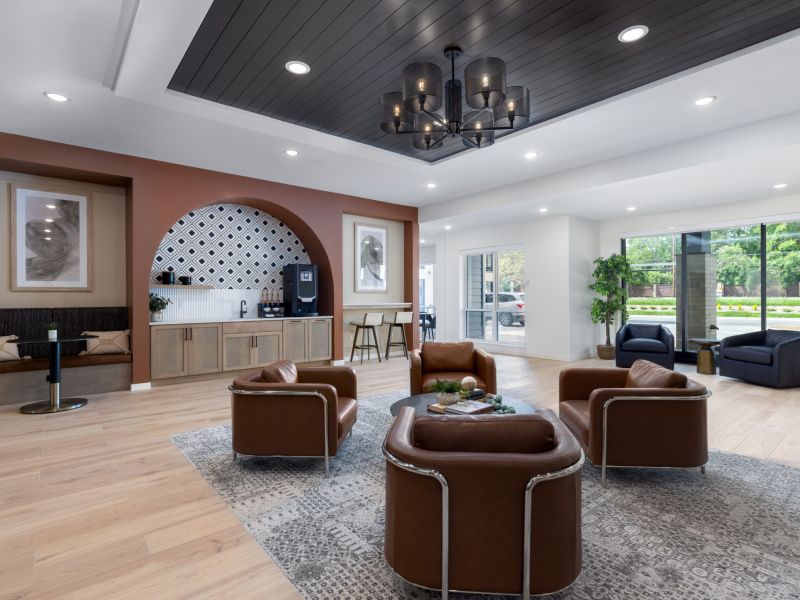 Modern lounge with brown leather chairs, coffee station, and large windows overlooking greenery.