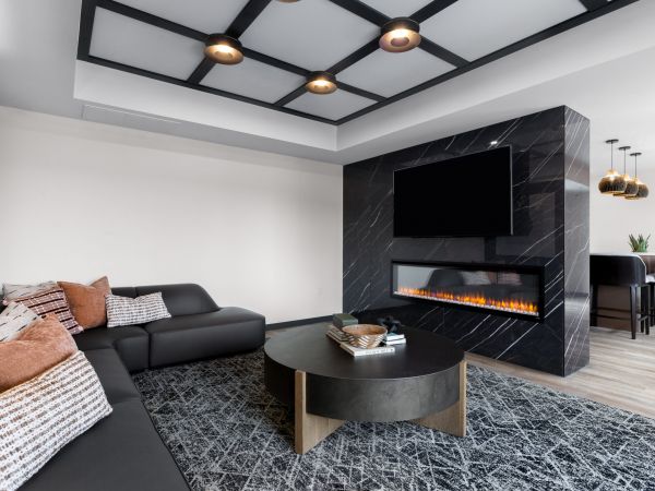 Modern living room with a black sectional sofa, round coffee table, fireplace, and wall-mounted TV.